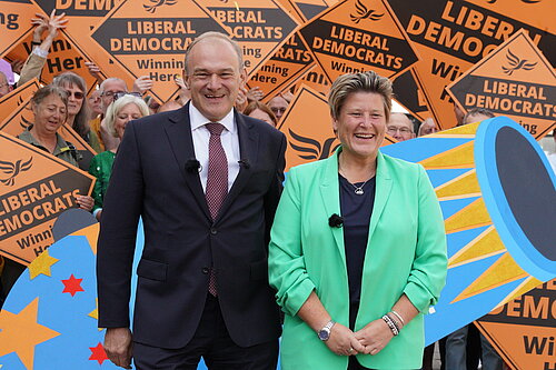 MP Ed Davey stood with MP Sue Dyke at her Parliamentary Victory Rally in Somerton and Frome, in front of a giant cardboard cutout of a celebration canon and surrounded by Lib Dem Activists holding Lib Dem orange placards, in 2023